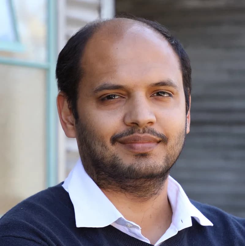 Portrait of Postman co-founder Abhinav Asthana wearing a dark sweater over a white collared shirt