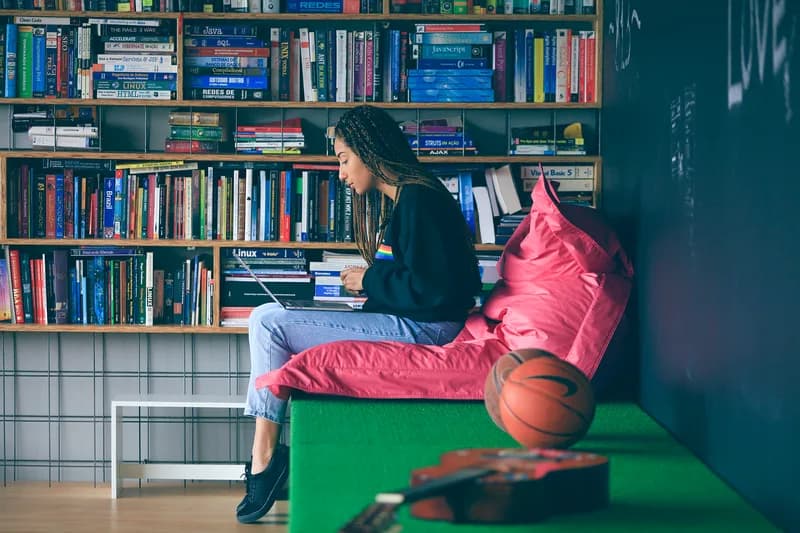 Thoughtworks employee working on a laptop on a beanbag in front of shelves of programming books in a Brazil office