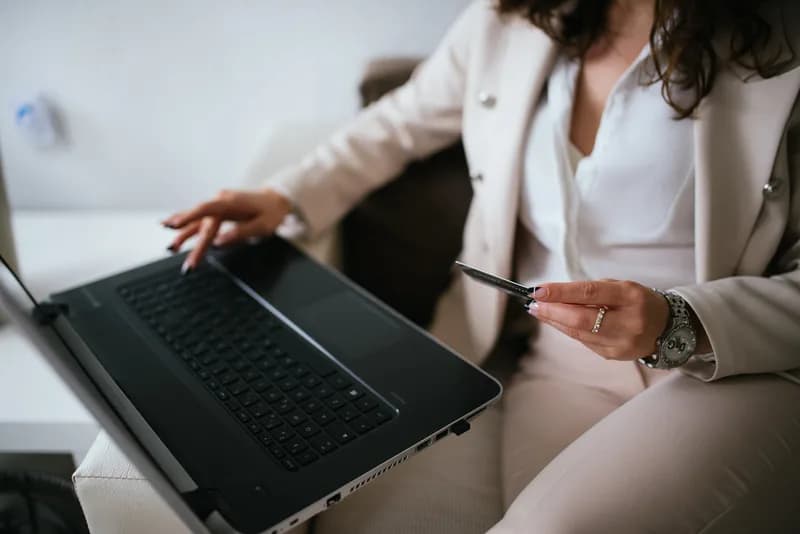 Person at a home desk holding a credit card while shopping online on a laptop