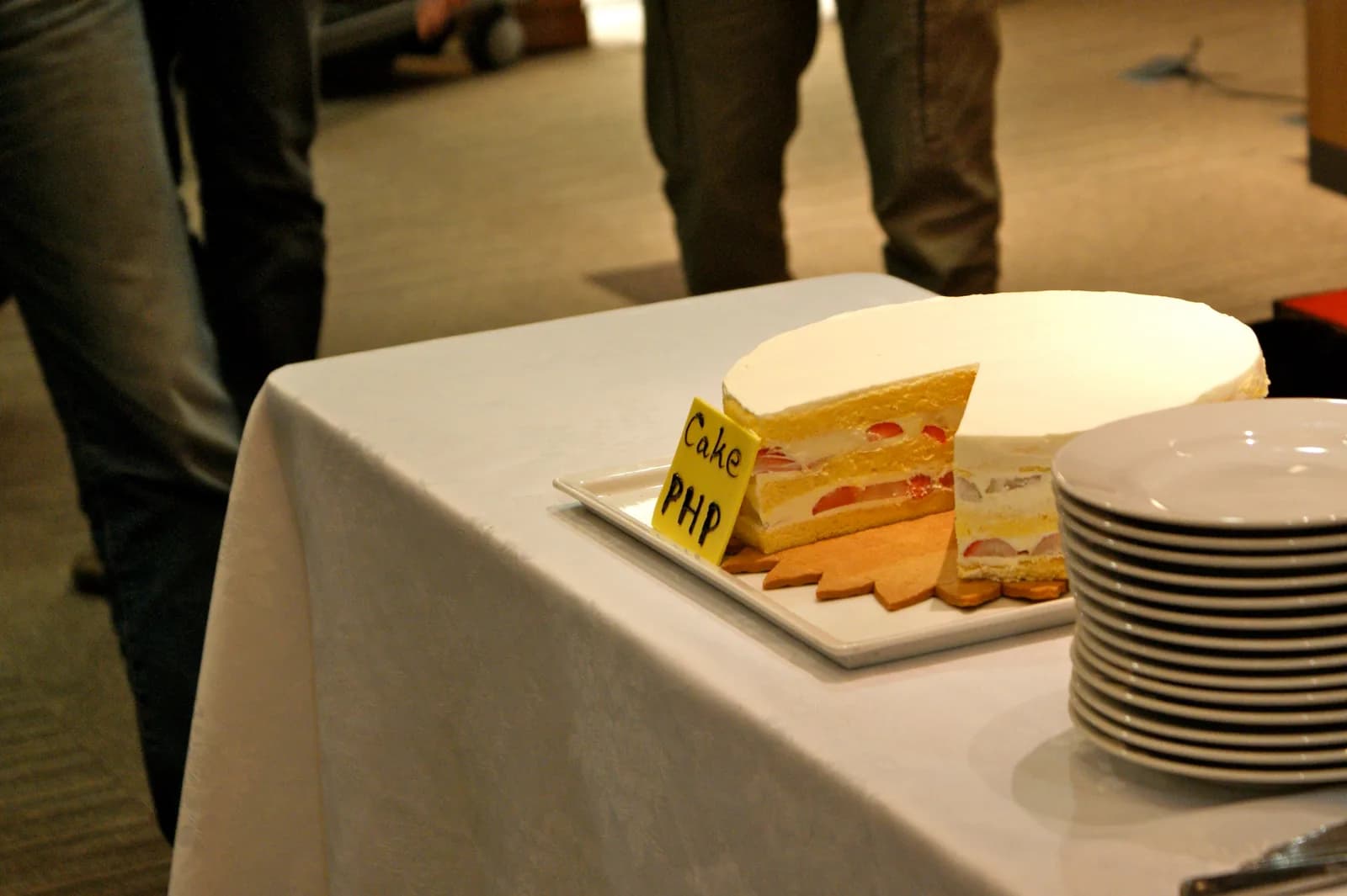 A sliced strawberry sponge cake with a handwritten Cake PHP label on a white buffet table