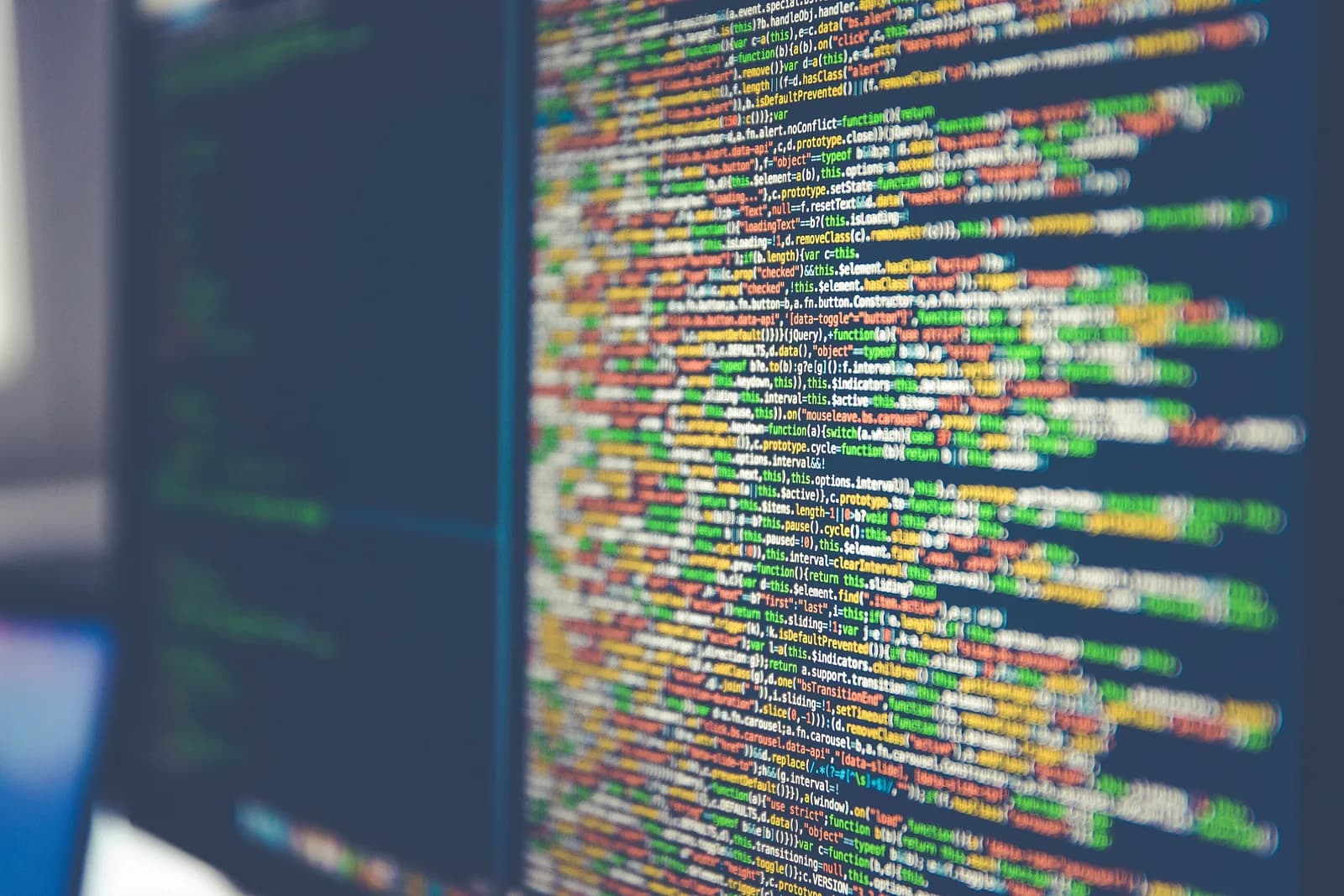 Computer monitor filled with colourful lines of source code photographed at an angle