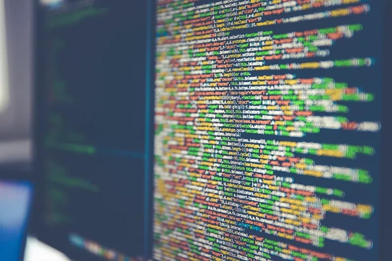 Computer monitor filled with lines of colourful source code in a dark editor theme