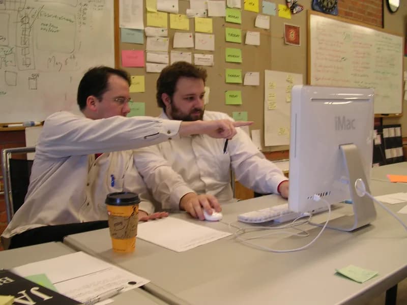 Two developers at a desk looking at a computer screen while one points at the code