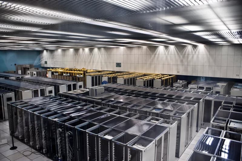 Rows of servers in tall racks inside a data centre with cabling overhead
