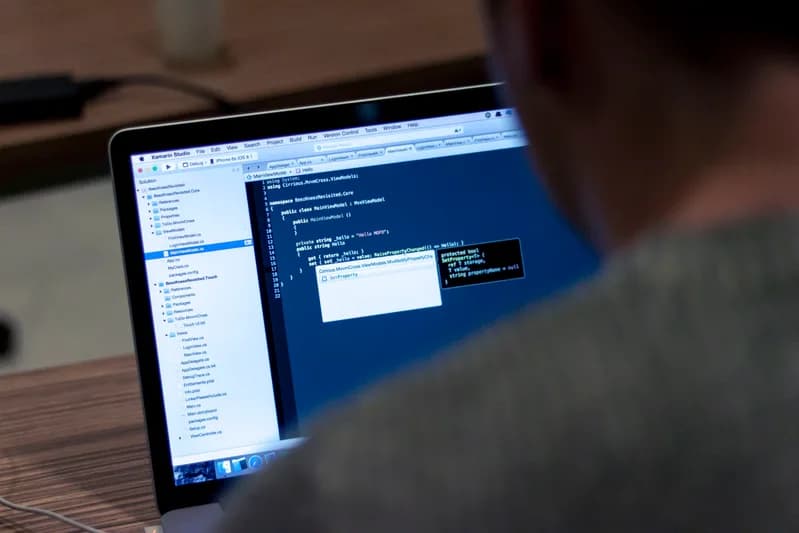 Developer's laptop on a wooden desk with a code editor open next to a notebook