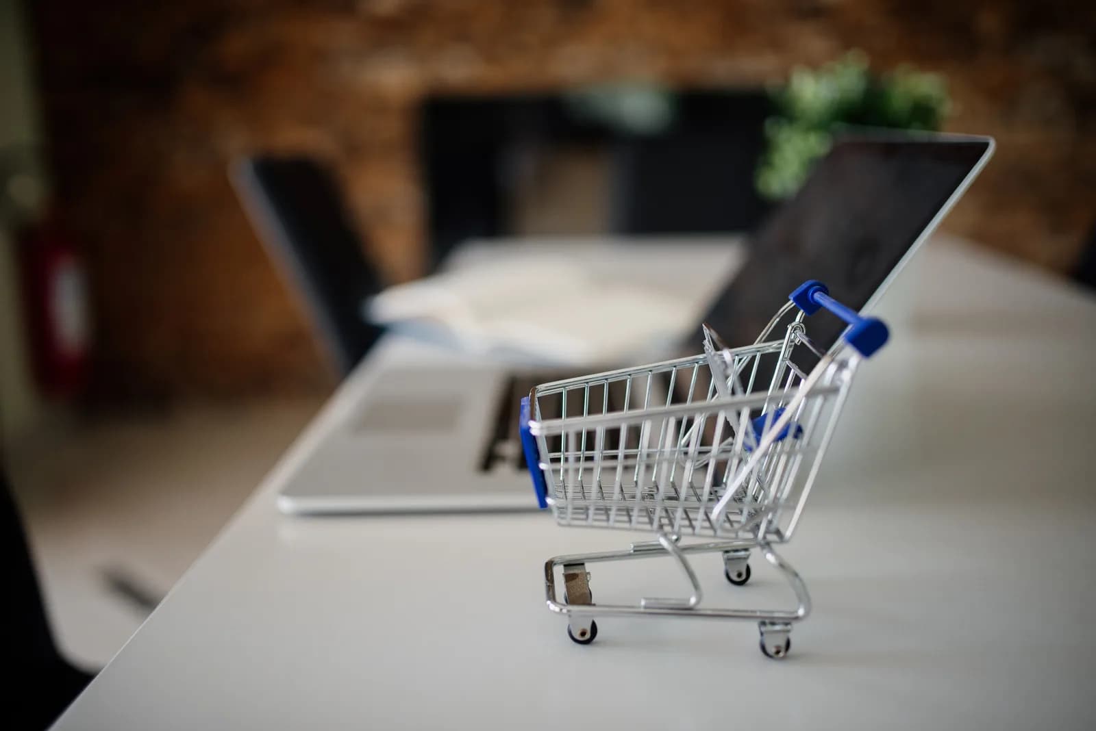 A miniature shopping cart placed on an office desk next to an open laptop