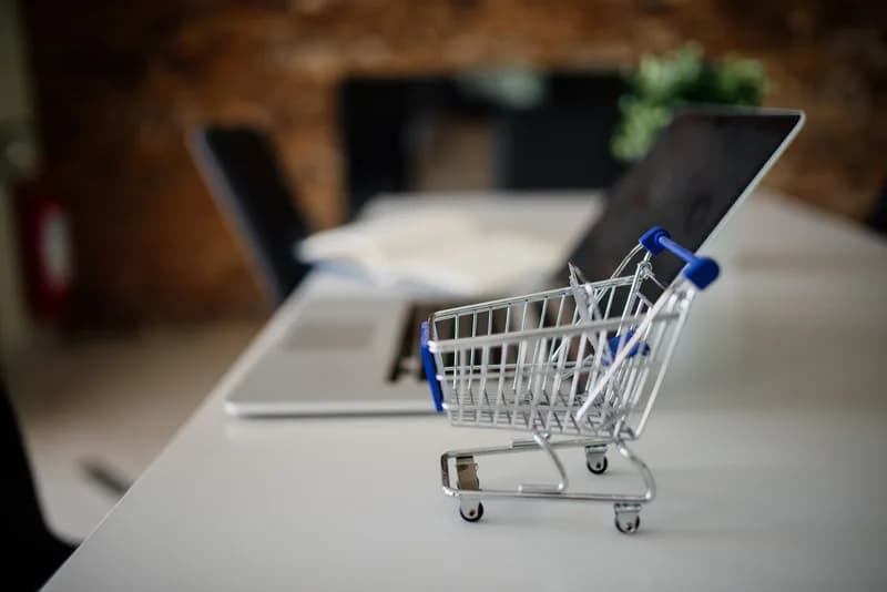 A miniature shopping cart placed on an office desk next to an open laptop