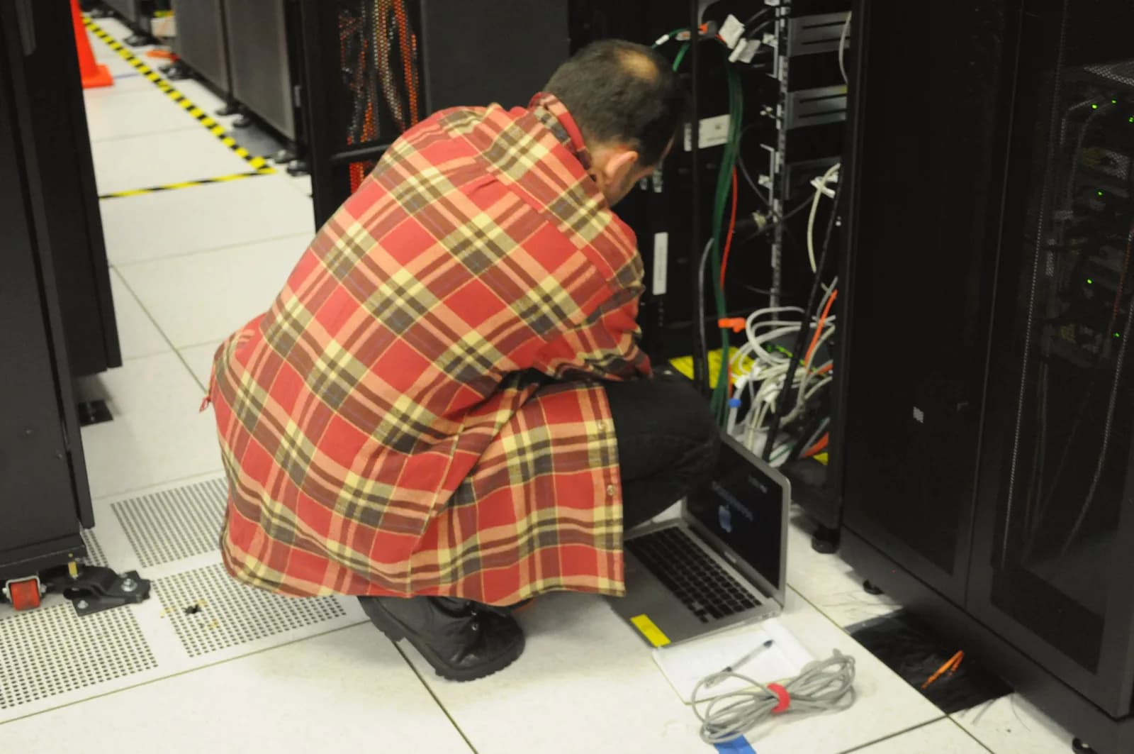 A technician holding a laptop while working at an open server rack in a data centre