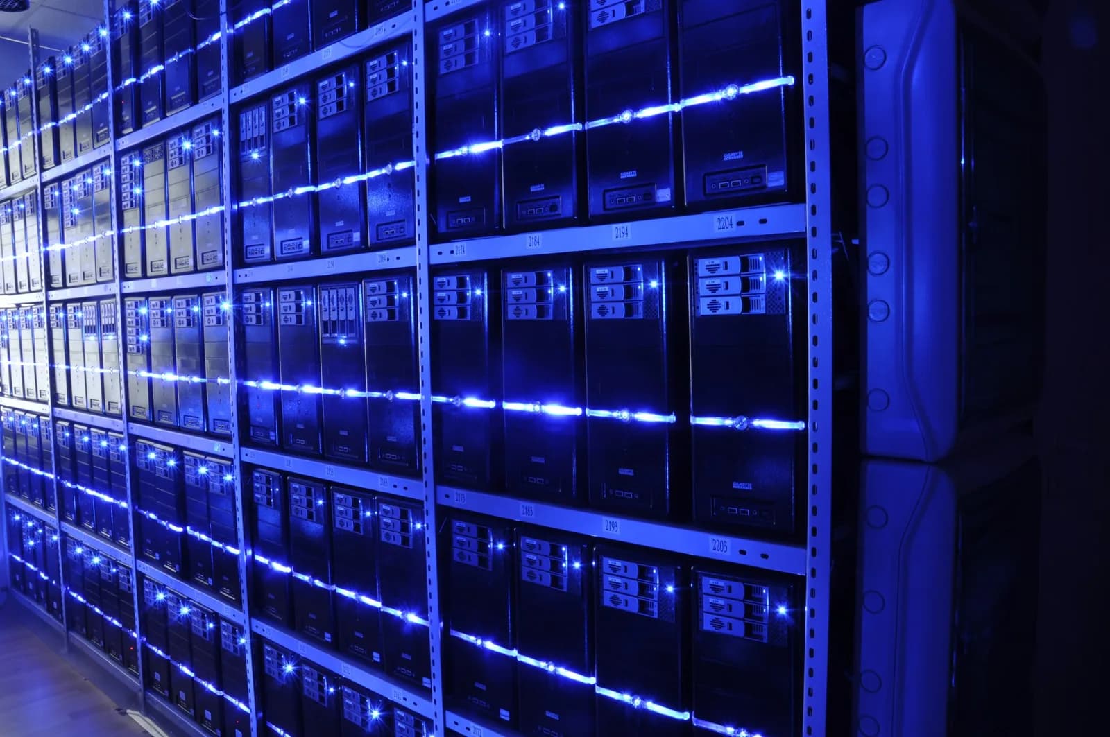 Aisle of a server room with rows of black server racks and cable trays under bright lighting