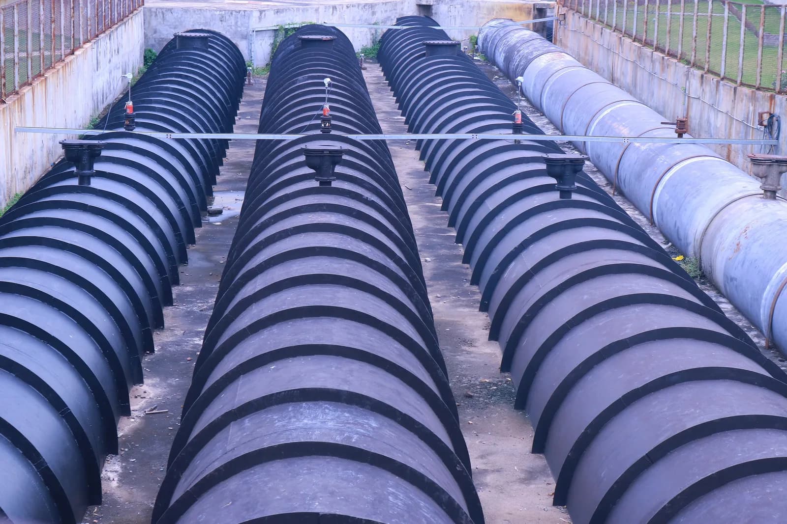 Rows of large black ribbed underground water tanks connected by pipelines in an industrial site