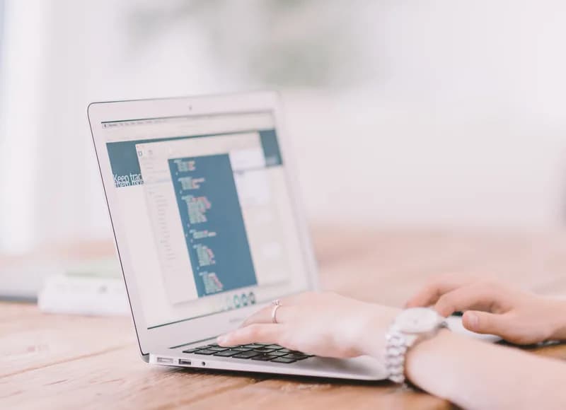 Hands typing on a laptop keyboard while the screen shows lines of code in a text editor