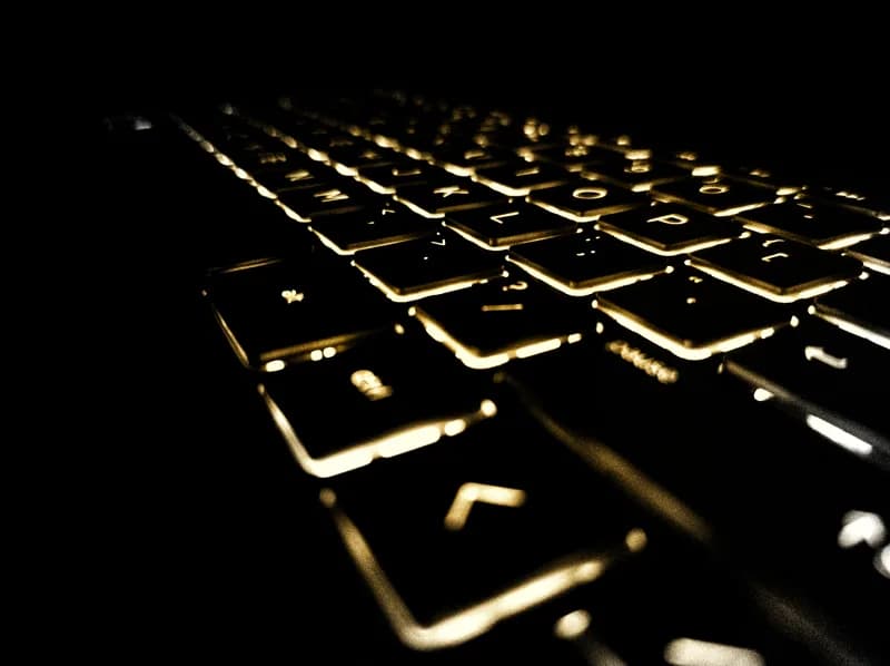 Backlit laptop keyboard glowing amber in a dark room, photographed at a low angle