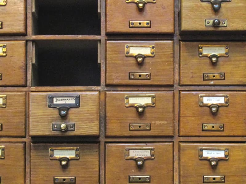 Wooden card catalogue drawers with brass handles and handwritten labels at the John Rylands Library, two drawers removed