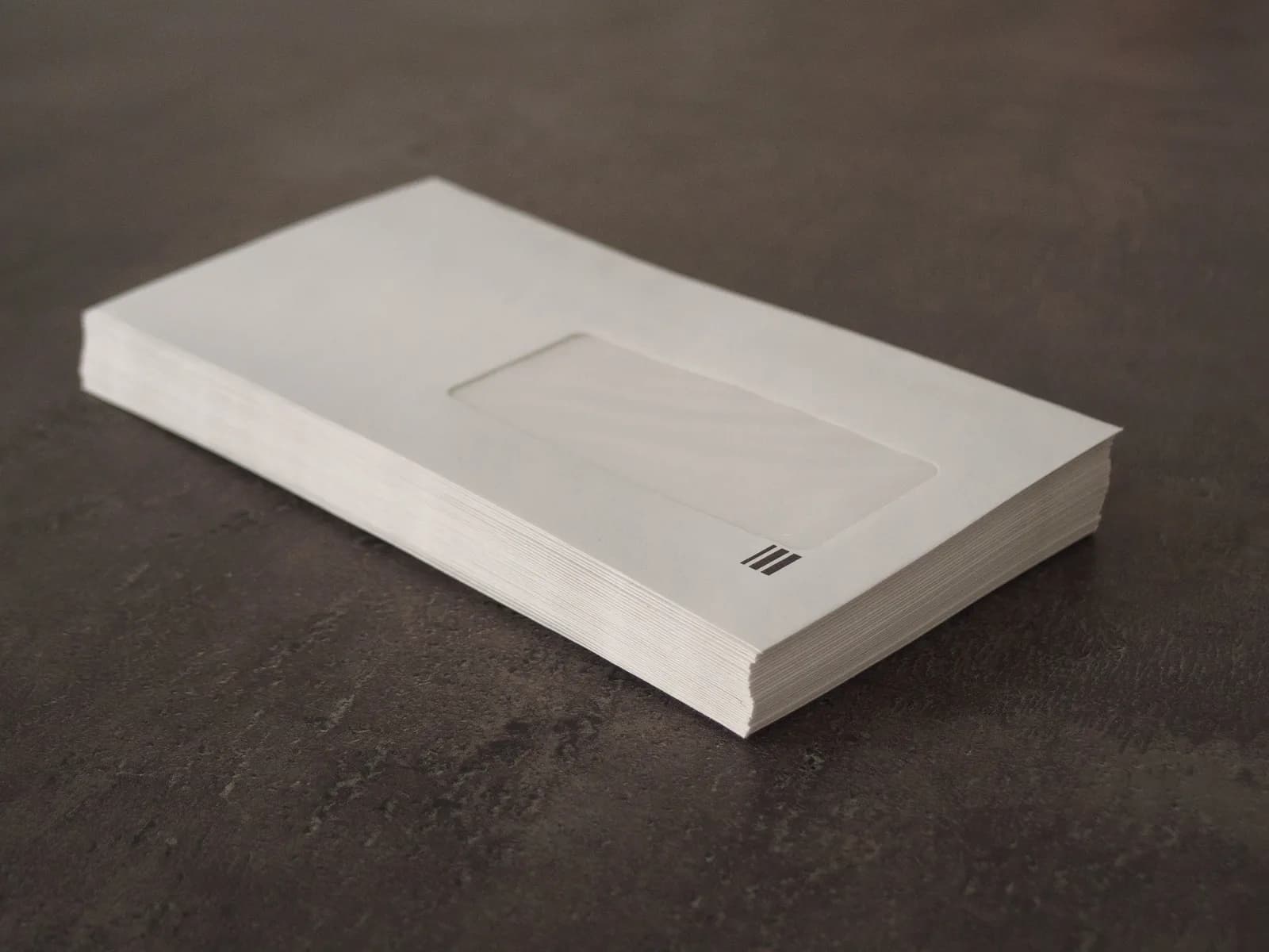 Stack of plain white window envelopes on a dark grey surface