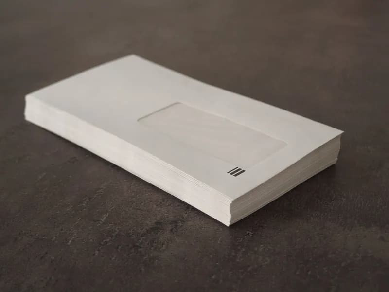 Stack of plain white window envelopes on a dark grey surface