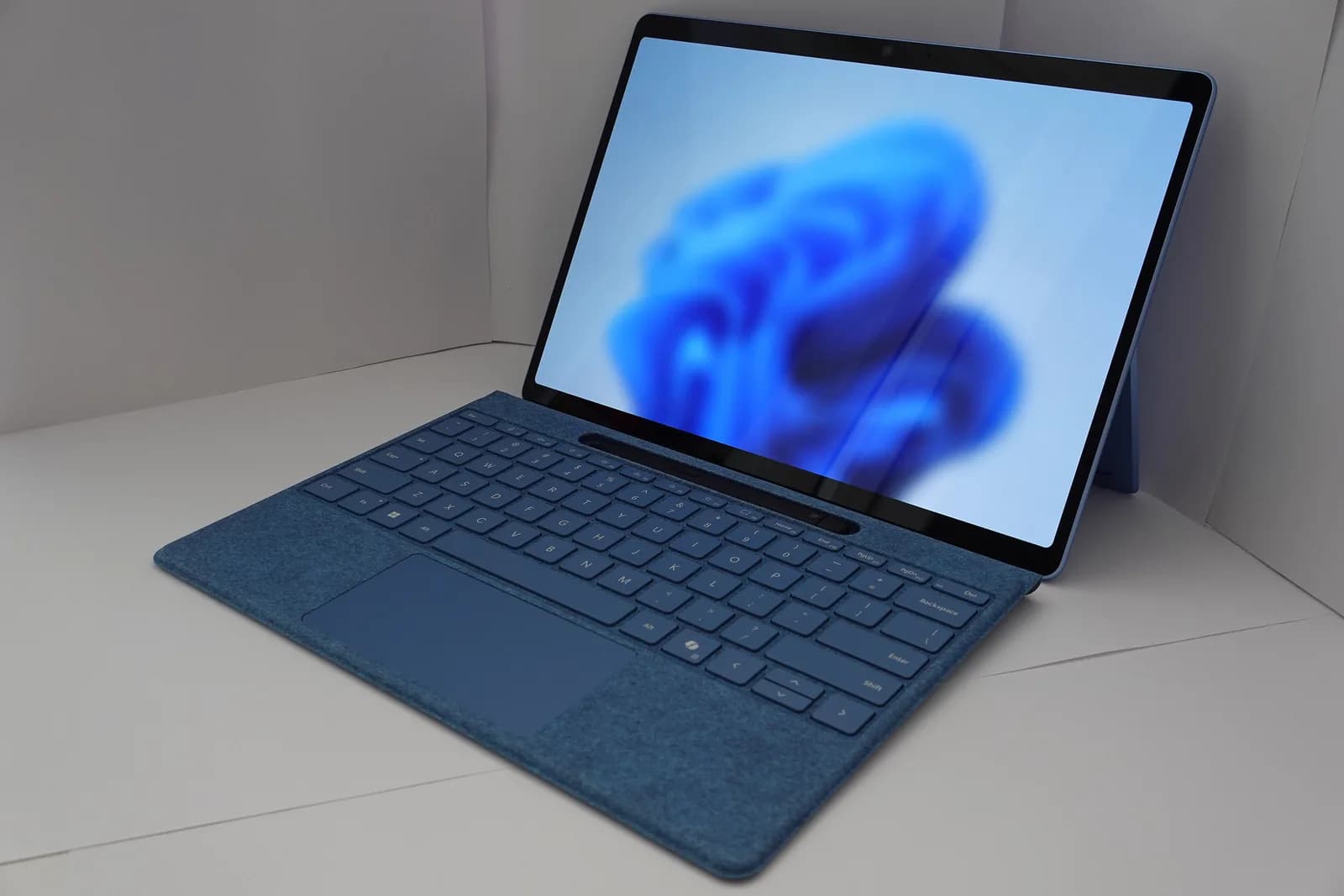 Blue two-in-one Windows laptop with a fabric keyboard cover, showing the Windows 11 bloom wallpaper
