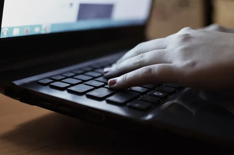 Close-up of a hand typing on a dark laptop keyboard in low light