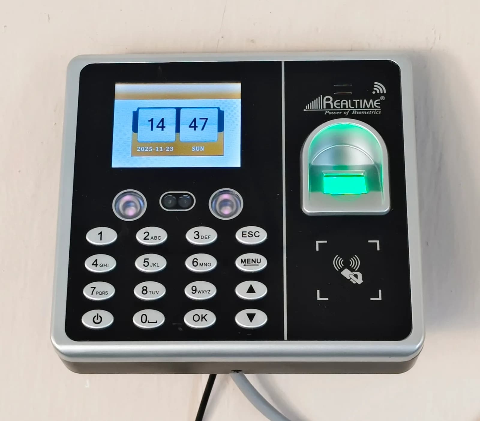 Wall-mounted access terminal with a keypad, a small screen and a glowing green fingerprint reader