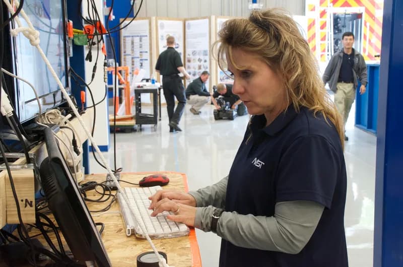Engineer typing at a test console keyboard in a robotics test facility with monitors and cables