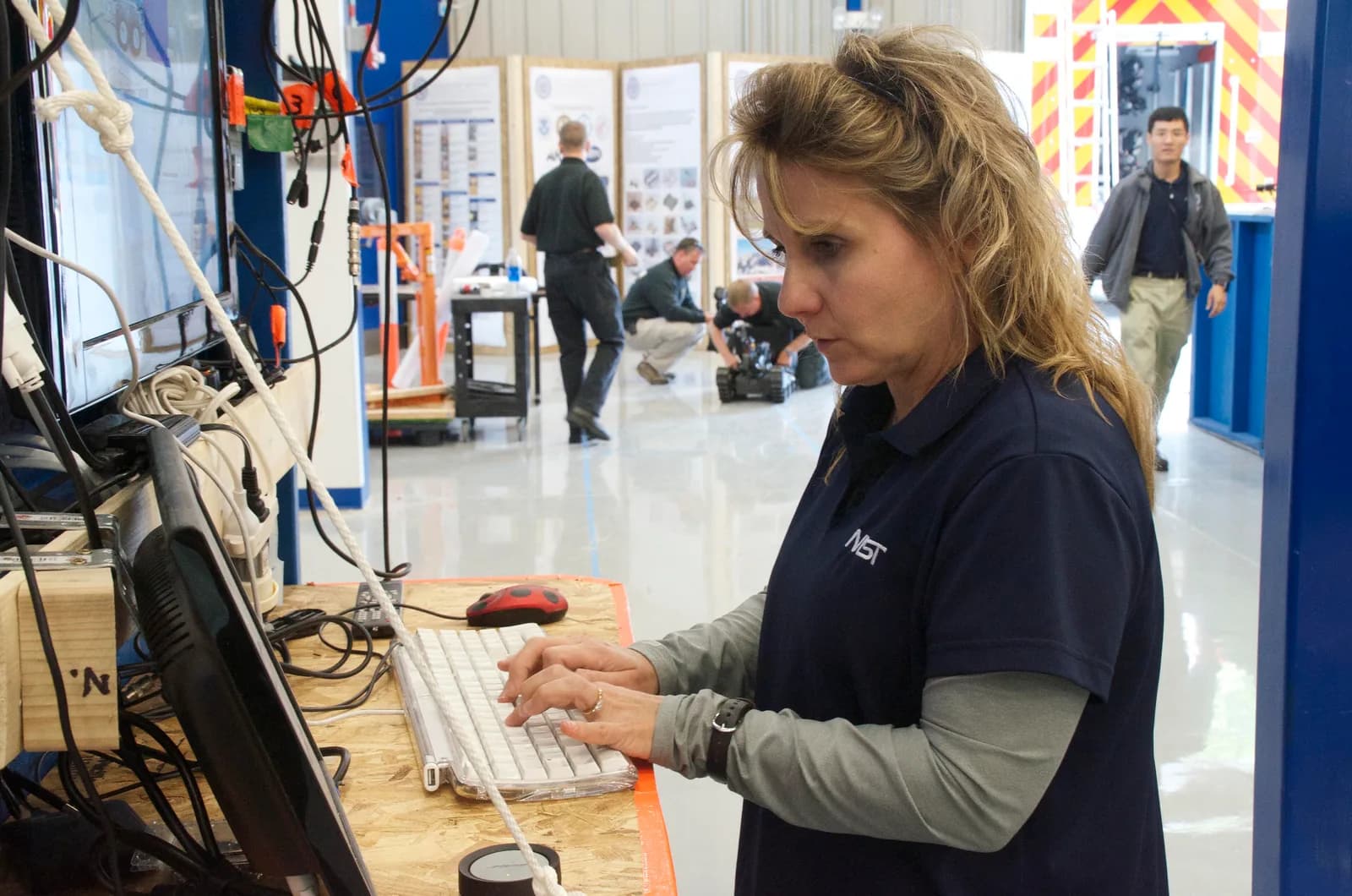 Engineer typing at a test console keyboard in a robotics test facility with monitors and cables