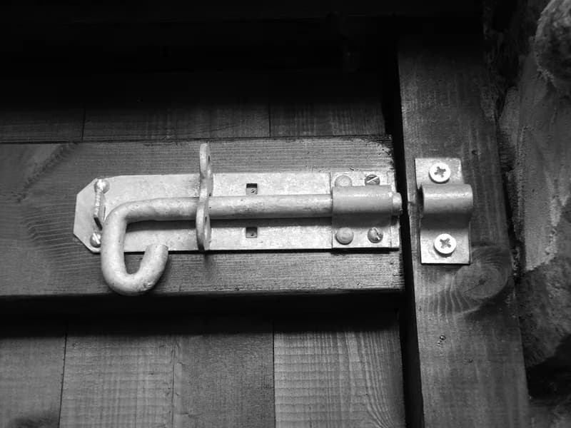 Black-and-white close-up of a galvanised barrel bolt fastening a wooden door to its frame