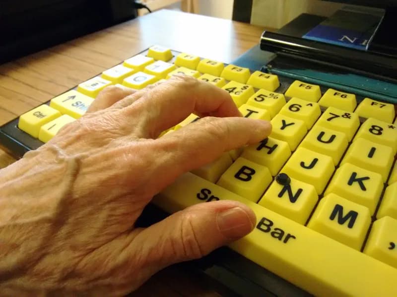 Hand of an older person typing on a large-print keyboard with black letters on bright yellow keys