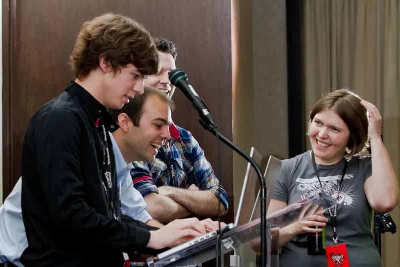 Developers gathered around a laptop at a lectern during a code competition at a JSConf event