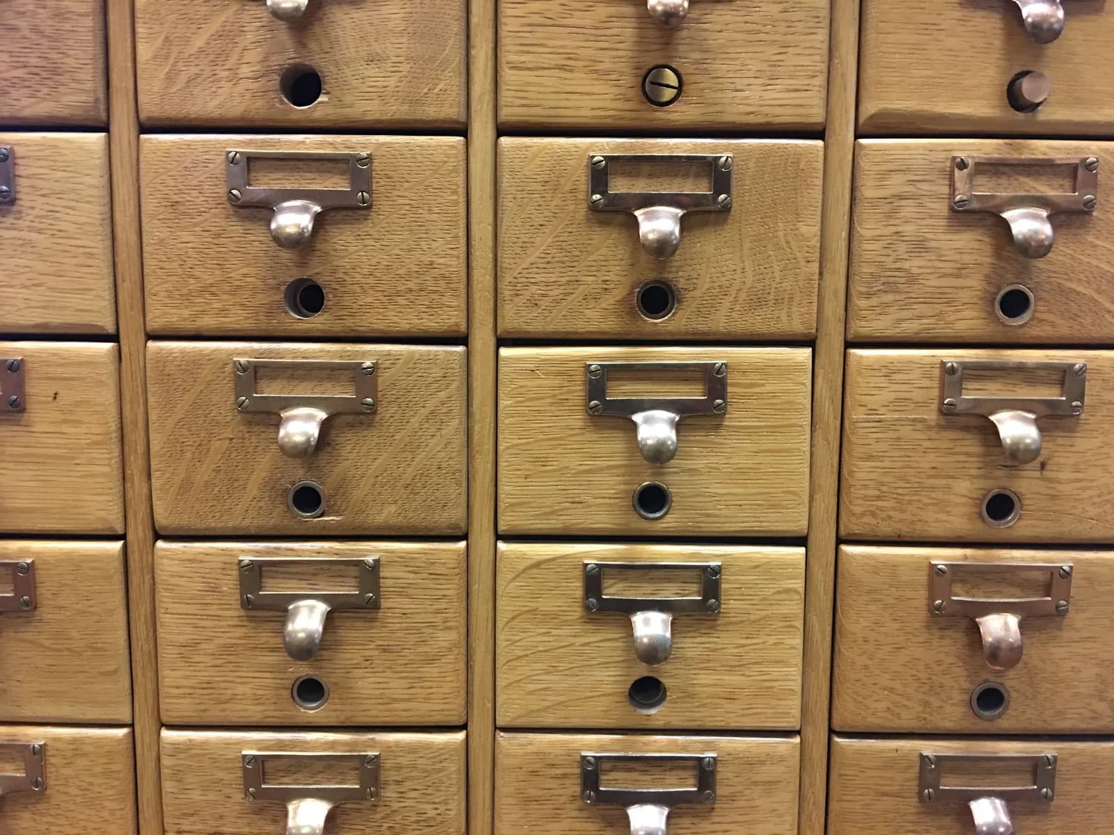 Close-up of wooden library card catalogue drawers with brass label holders and pull handles