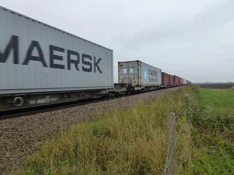 Long freight train of shipping containers on flat wagons passing through flat countryside