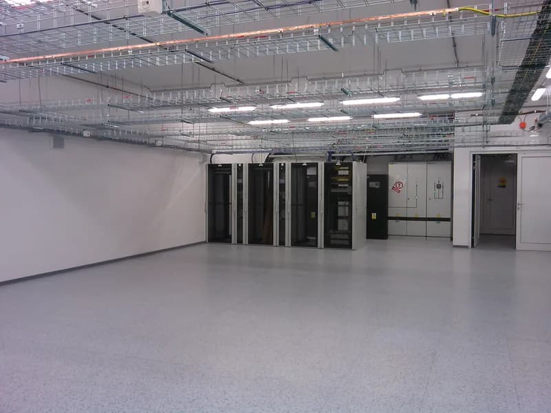 Row of five server cabinets in a large, bright data centre hall under overhead cable trays