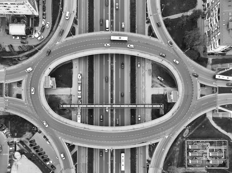 Black-and-white aerial view of an oval roundabout above a multi-lane road in Belgrade, with cars and buses circling the loop