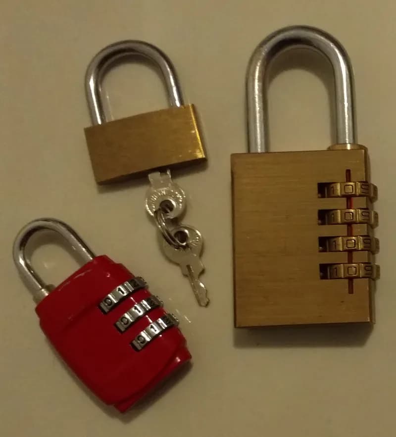 Three padlocks on a white surface: a red three-digit combination lock, a small brass lock with two keys and a larger brass four-digit combination lock