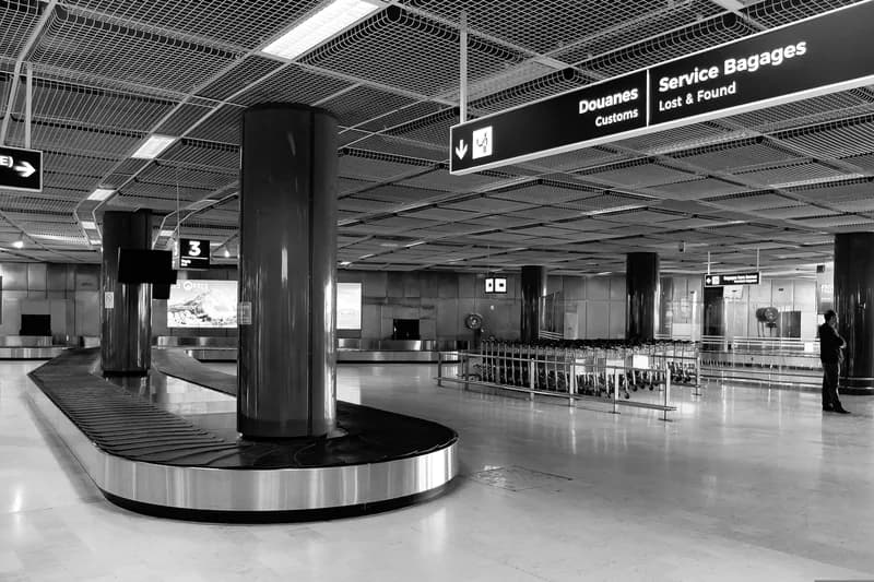 Black-and-white photo of an empty airport baggage carousel under a sign for customs and lost and found