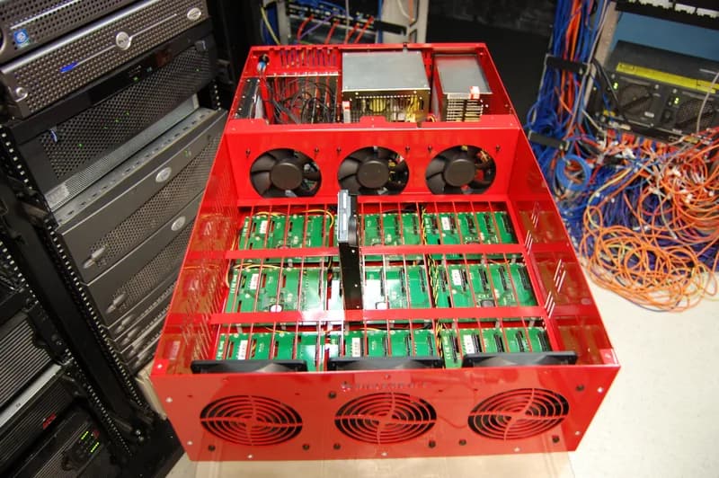 Open red storage pod chassis with rows of empty drive slots and cooling fans, next to server racks and coloured network cables