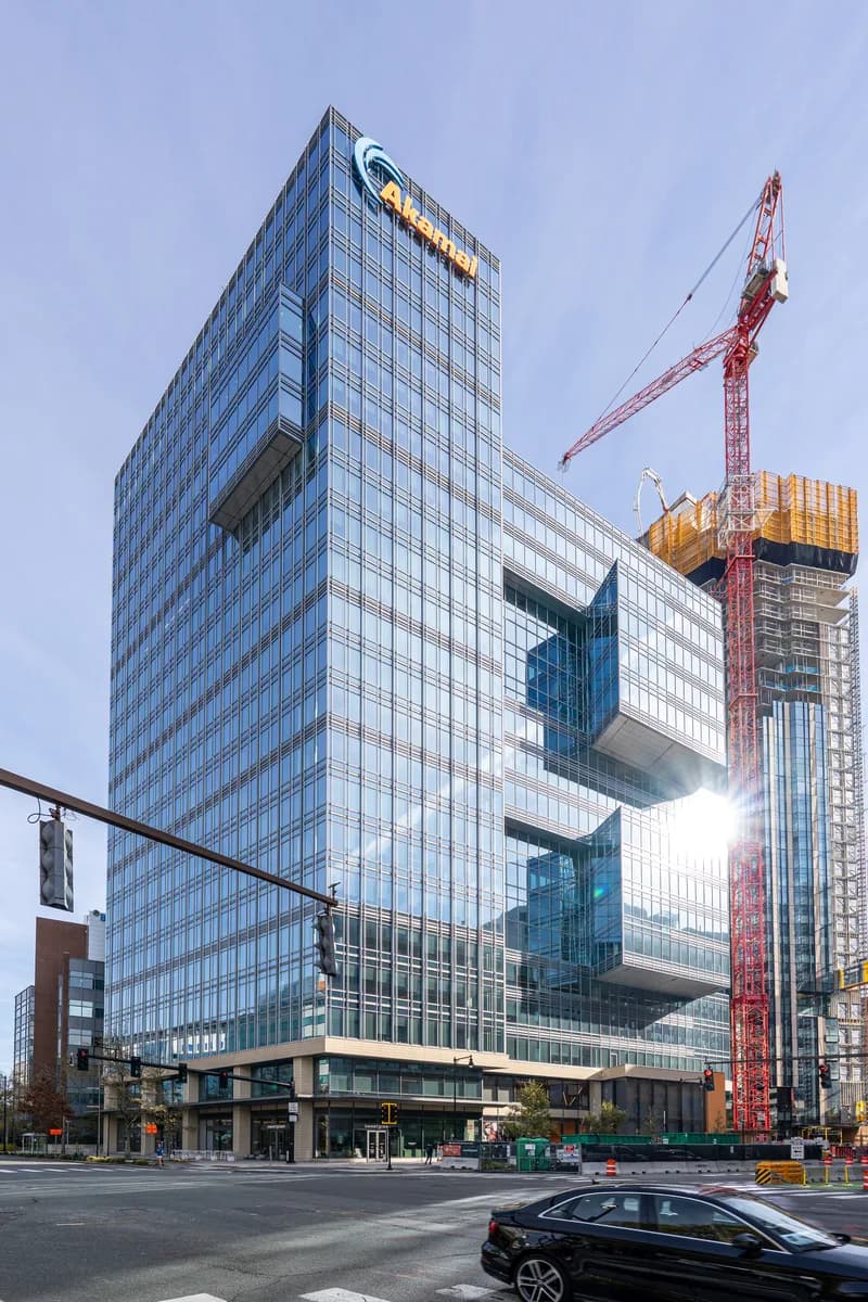 Glass office tower with the Akamai logo near the top at 145 Broadway in Cambridge, Massachusetts, beside a construction crane