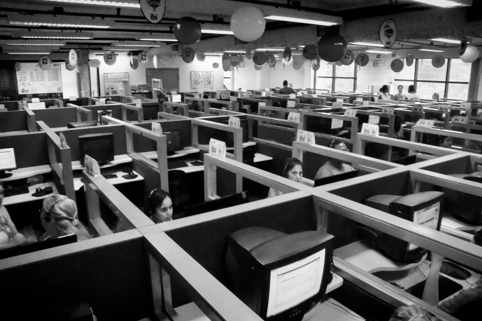 Black and white photo of a call centre in São Paulo with rows of cubicles, computer monitors and support agents wearing headsets at their desks