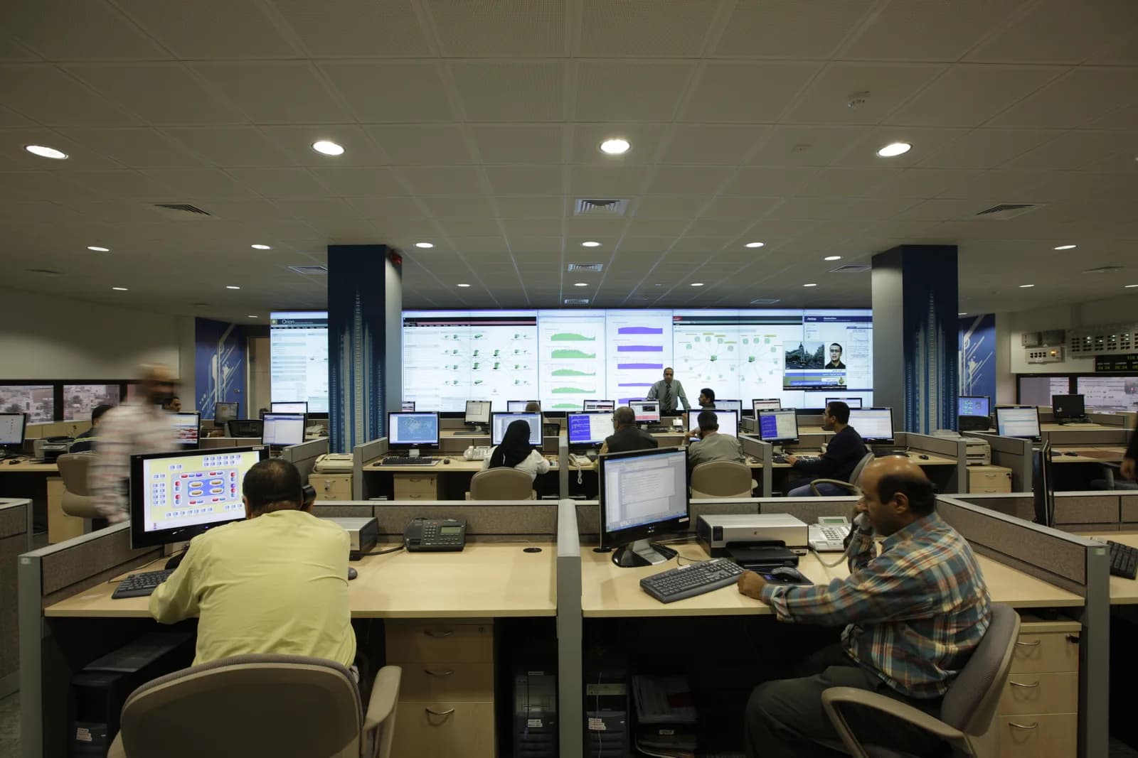 Staff at desks in a telecom network operations centre in Bahrain, facing a wall of large screens showing traffic graphs and network maps