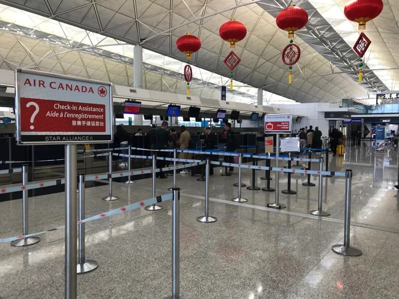 Air Canada check-in area at Hong Kong International Airport with a red Check-in Assistance sign, queue barriers and passengers at the desks