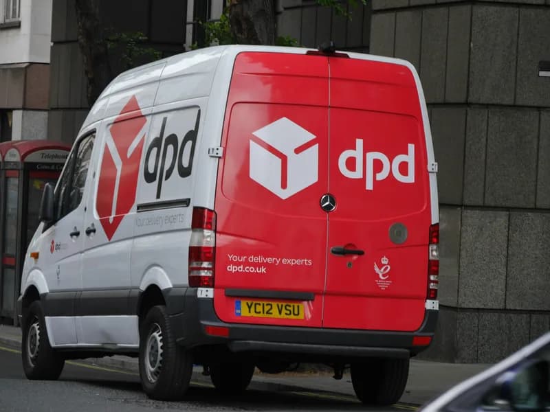 Rear view of a red and white DPD parcel delivery van parked on Monmouth Street in London's Covent Garden beside a stone building and a red telephone box