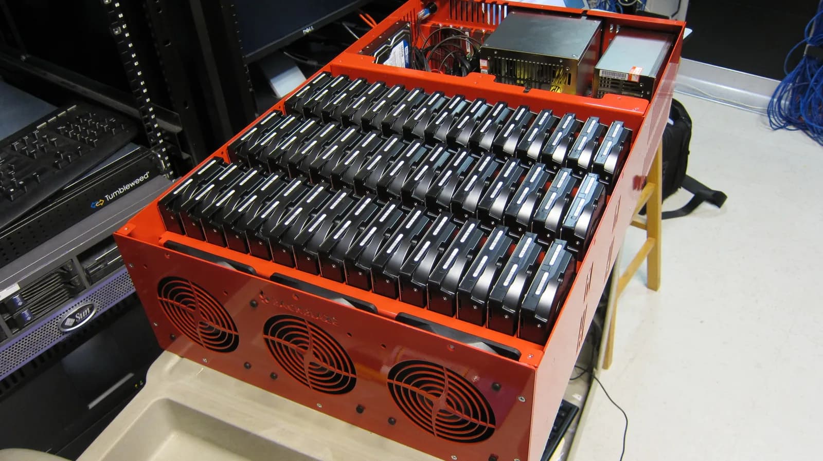 An open red Backblaze Storage Pod 2.0 chassis on a bench, filled with 45 hard drives in rows, with three cooling fans on the front panel