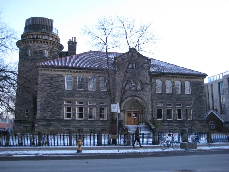 Stone Romanesque building housing the University of Toronto admissions office in winter, with a round tower, arched entrance and a person walking past