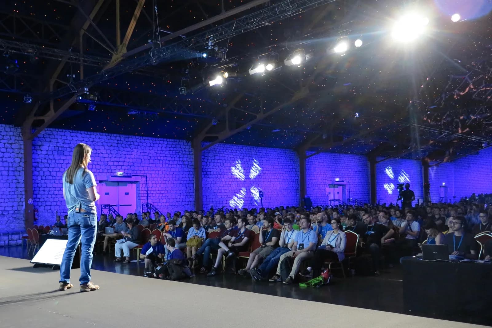 Alain Schlesser speaking on stage at WordCamp Europe 2017 in Paris to a large seated audience in a hall lit in purple and blue