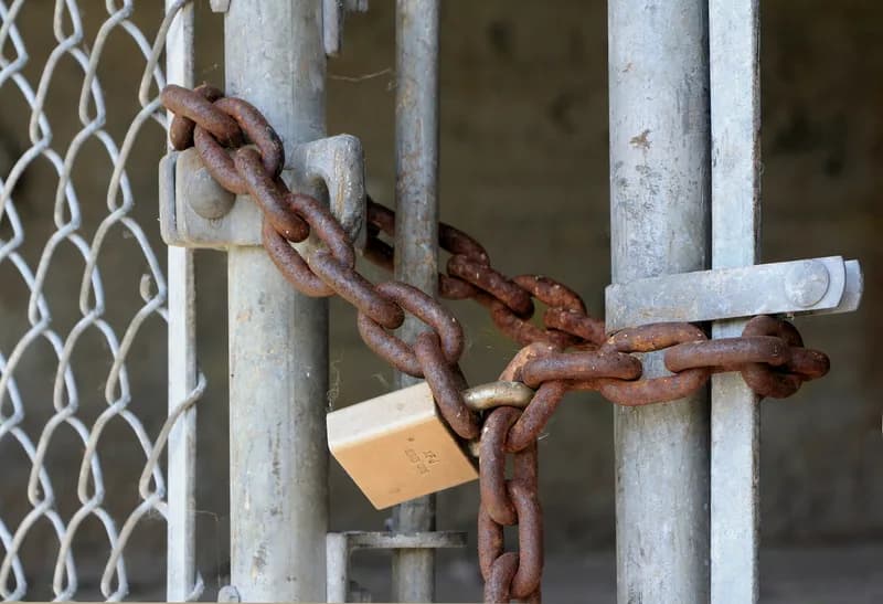 Padlock and rusty chain securing a metal gate.