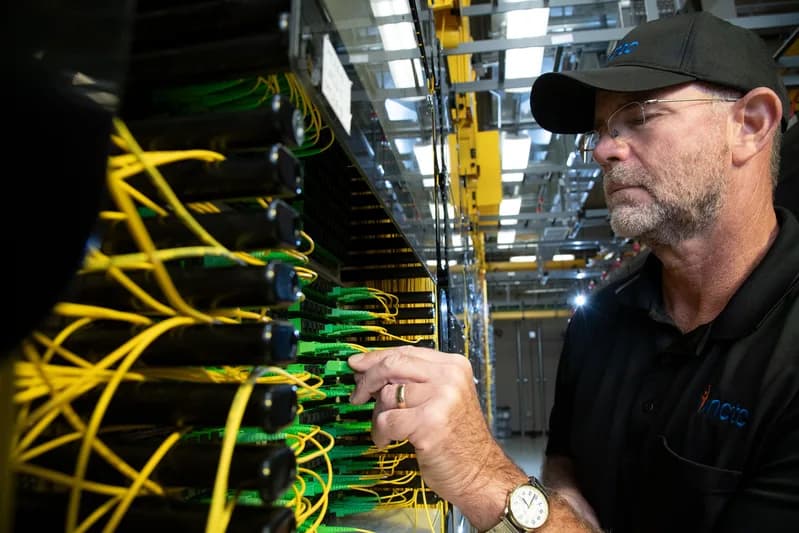 Technician connecting fibre cables in a network equipment rack.