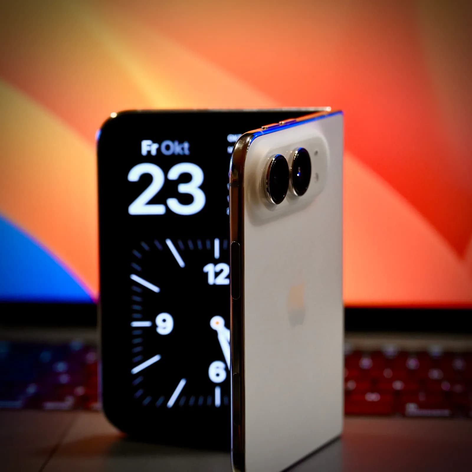 Half-open iPhone Duo showing the date and a clock beside a MacBook Pro.
